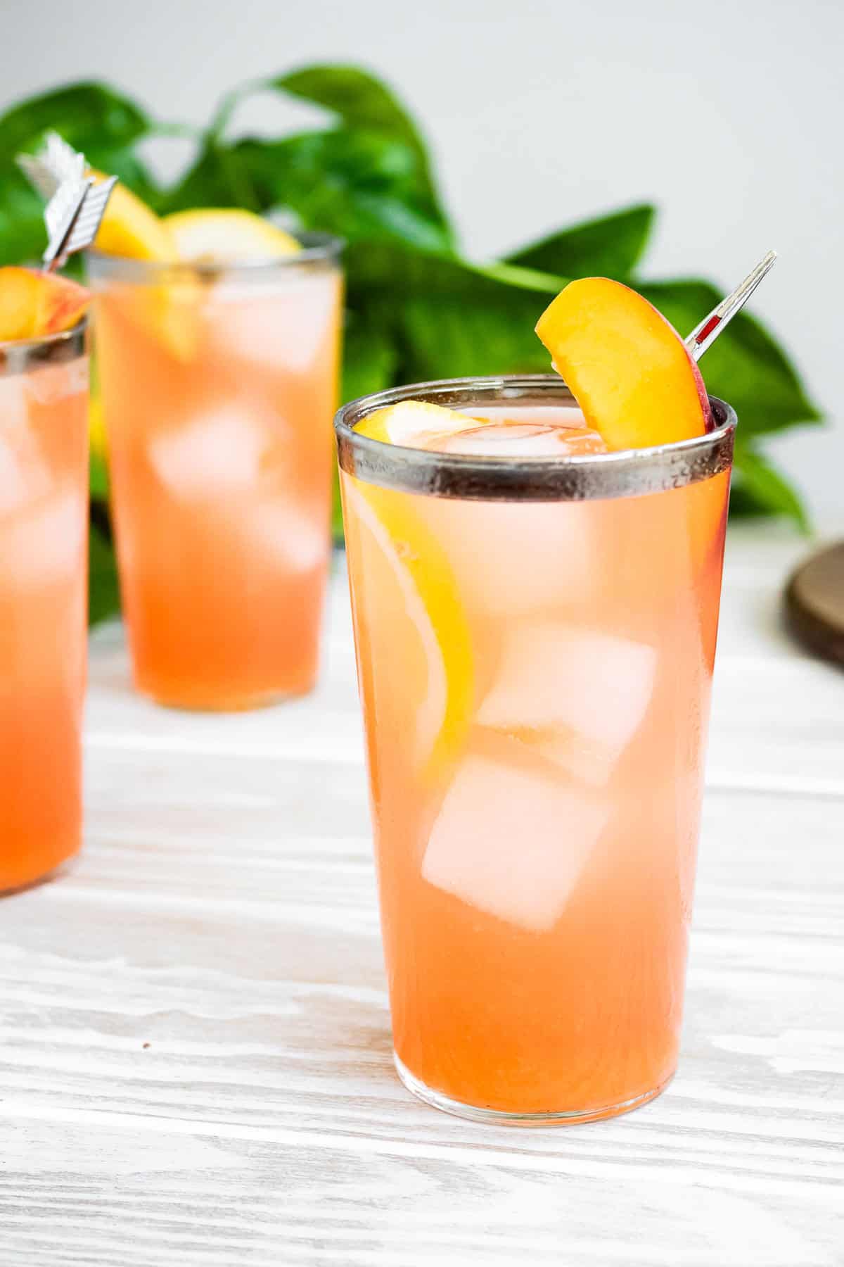 A close up of a glass of peach lemonade in front of 2 more glasses of the lemonade.