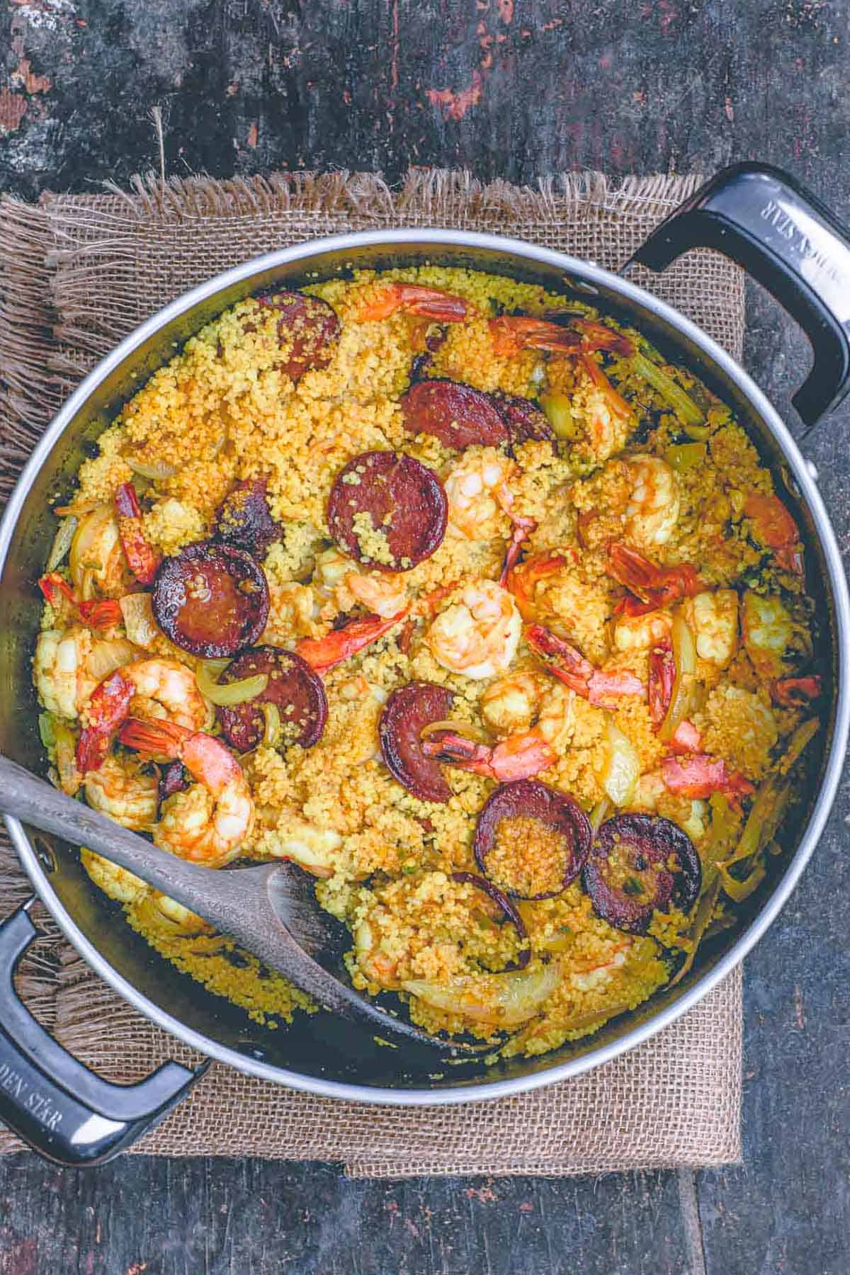 An overhead photo of shrimp couscous in a pot with a wooden spoon.