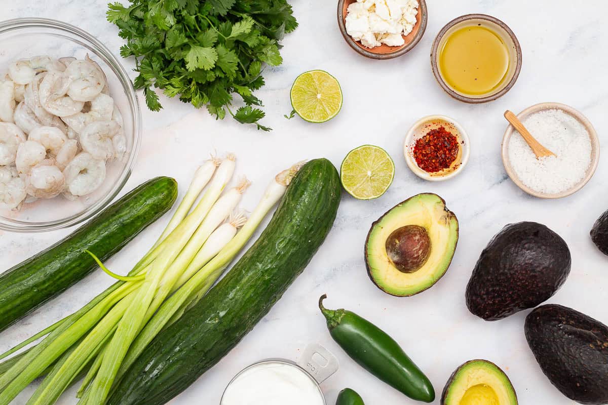 Ingredients for avocado soup including avocados, cucumber, jalapeno, lime, greek yogurt, cilantro, salt, olive oil, shrimp and aleppo pepper.