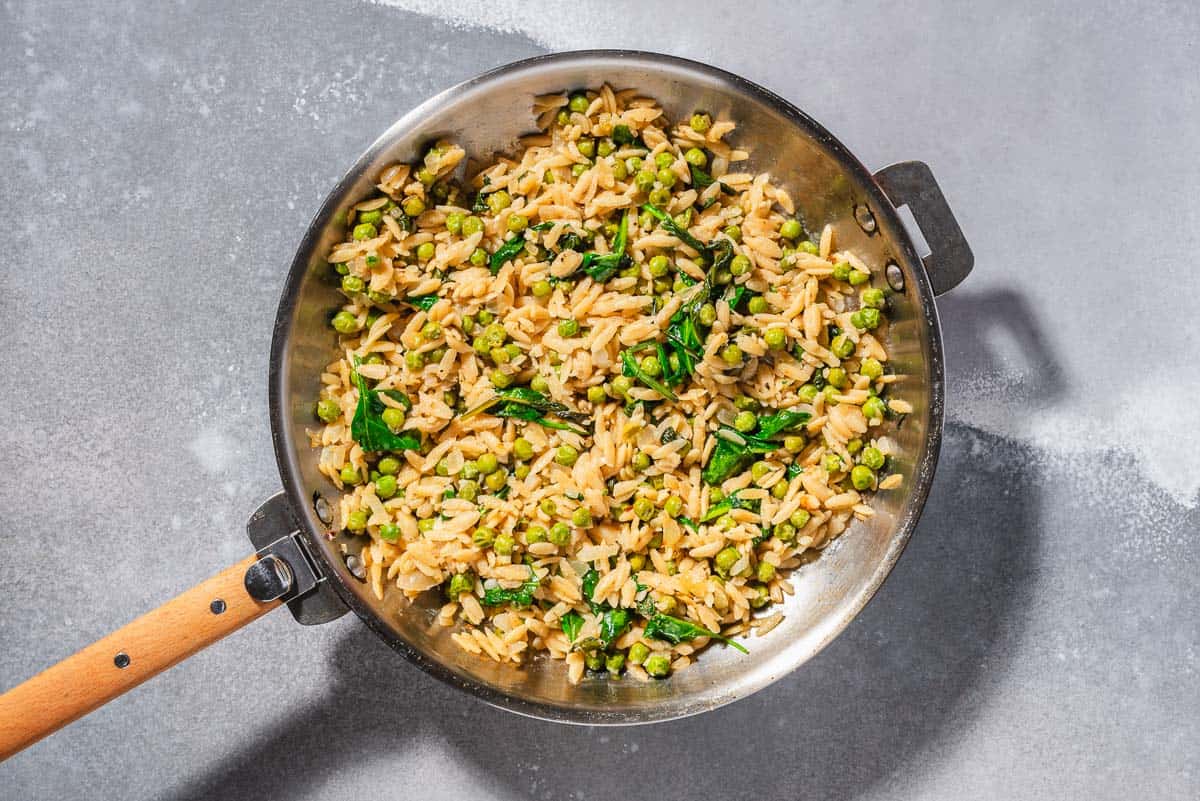 An overhead photo of the orzo, onion, peas and spinach in a skillet.