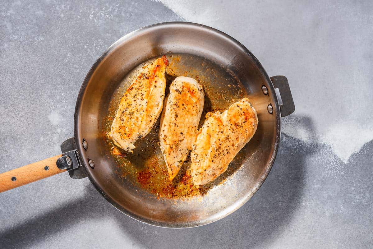 An overhead photo of 3 chicken breasts being seared in a skillet