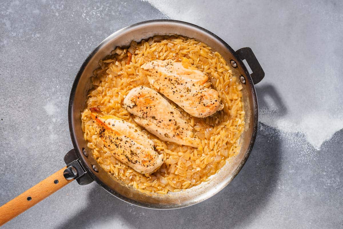 An overhead photo of the onion, orzo and chicken cooking in a skillet.