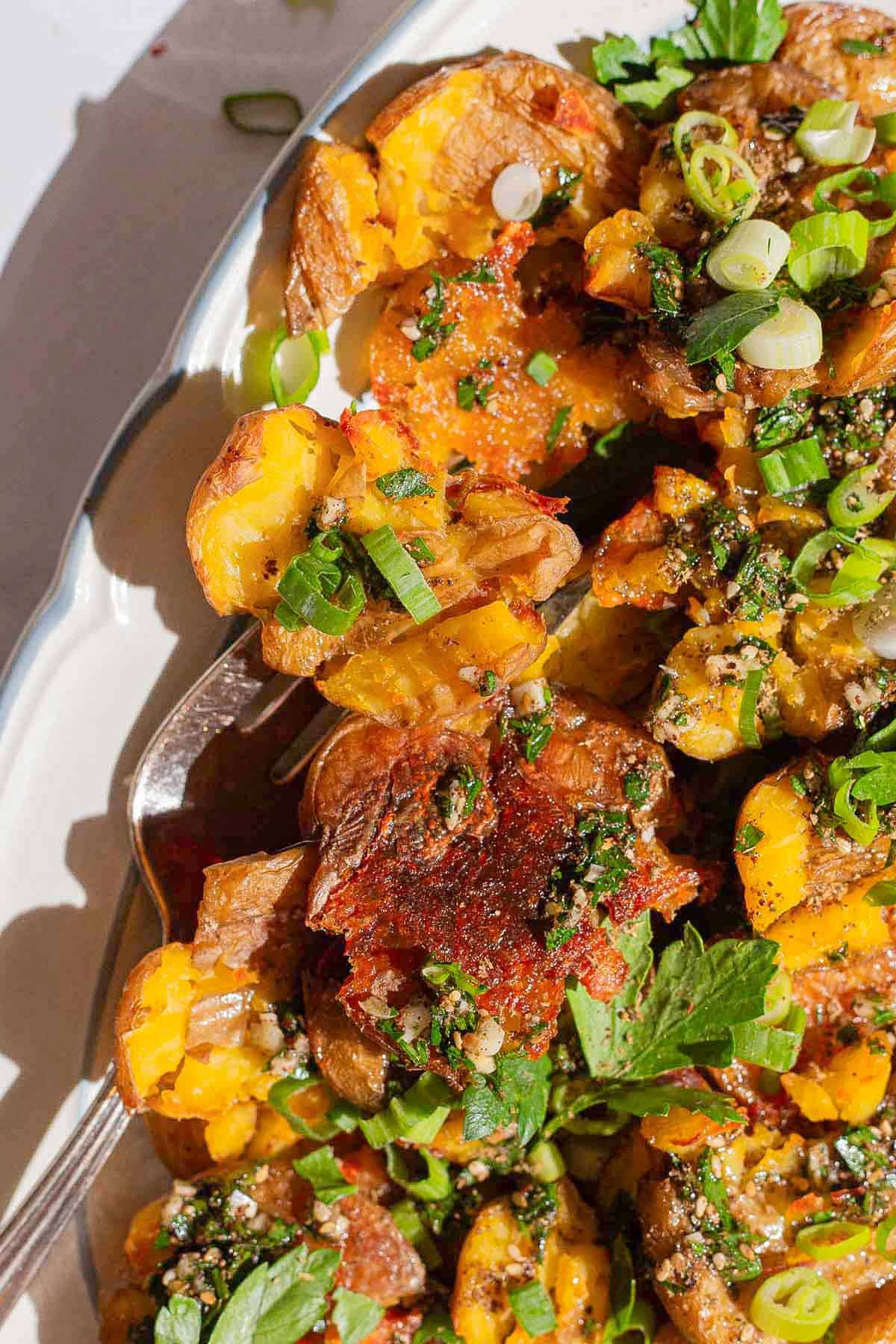 A close up of crispy smashed potatoes on a serving platter with a fork.