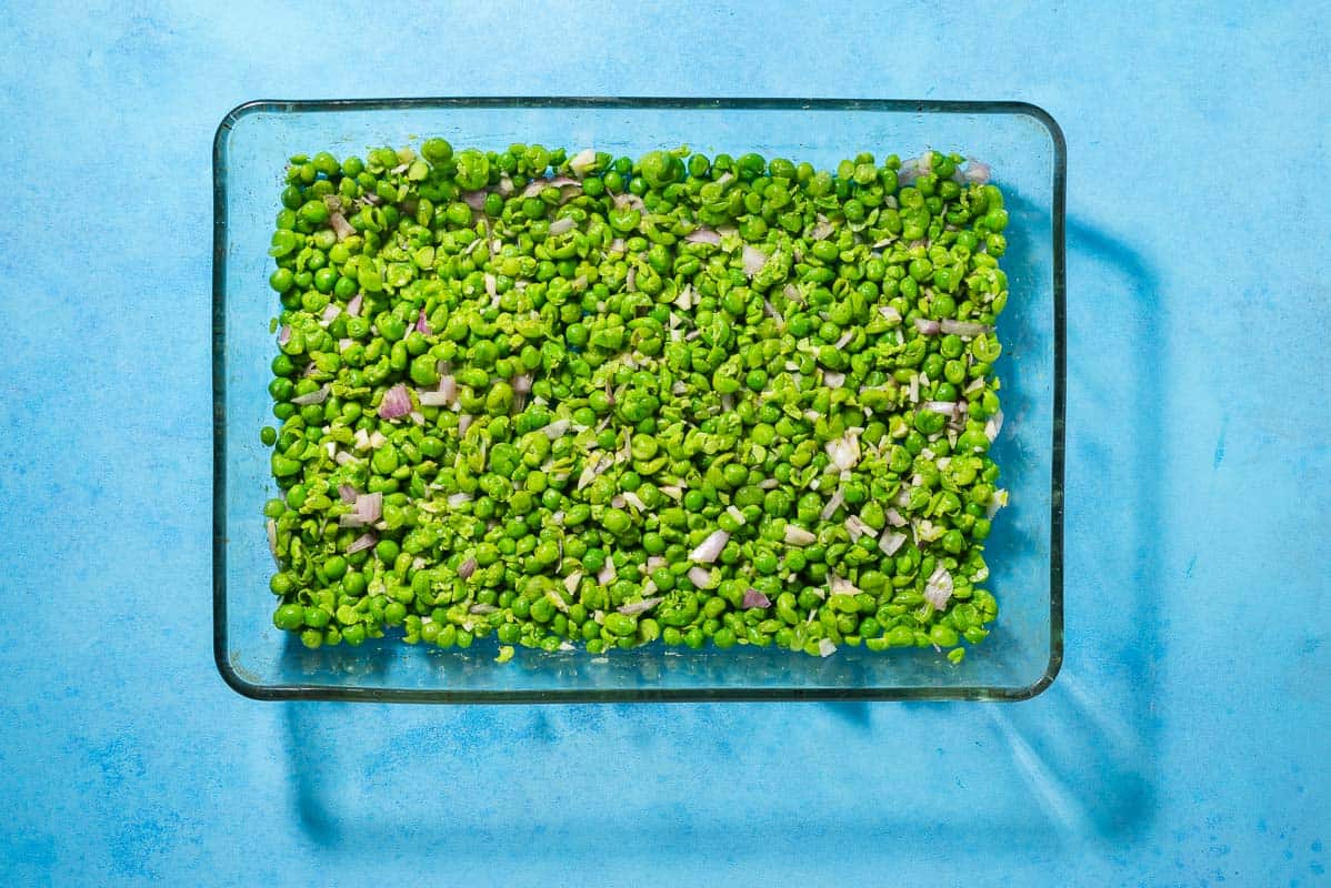 An overhead photo of a baking dish with smashed peas spread on the bottom.