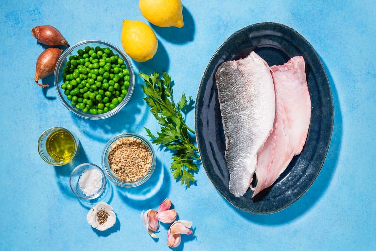 Ingredients for baked white fish including chilean sea bass fillets, lemons, olive oil, peas, salt, pepper, shallots, dukkah, garlic and parsley.