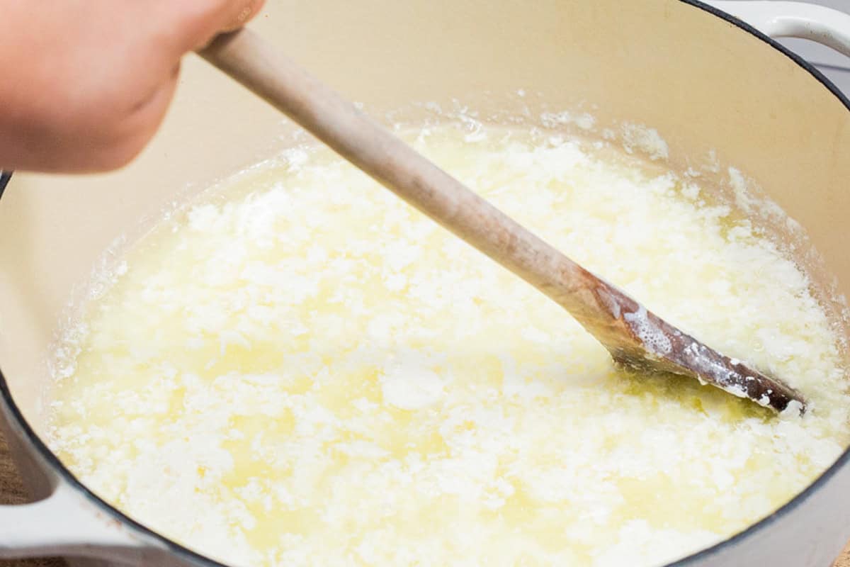 A close up of curds forming in a large pot with a wooden spoon.