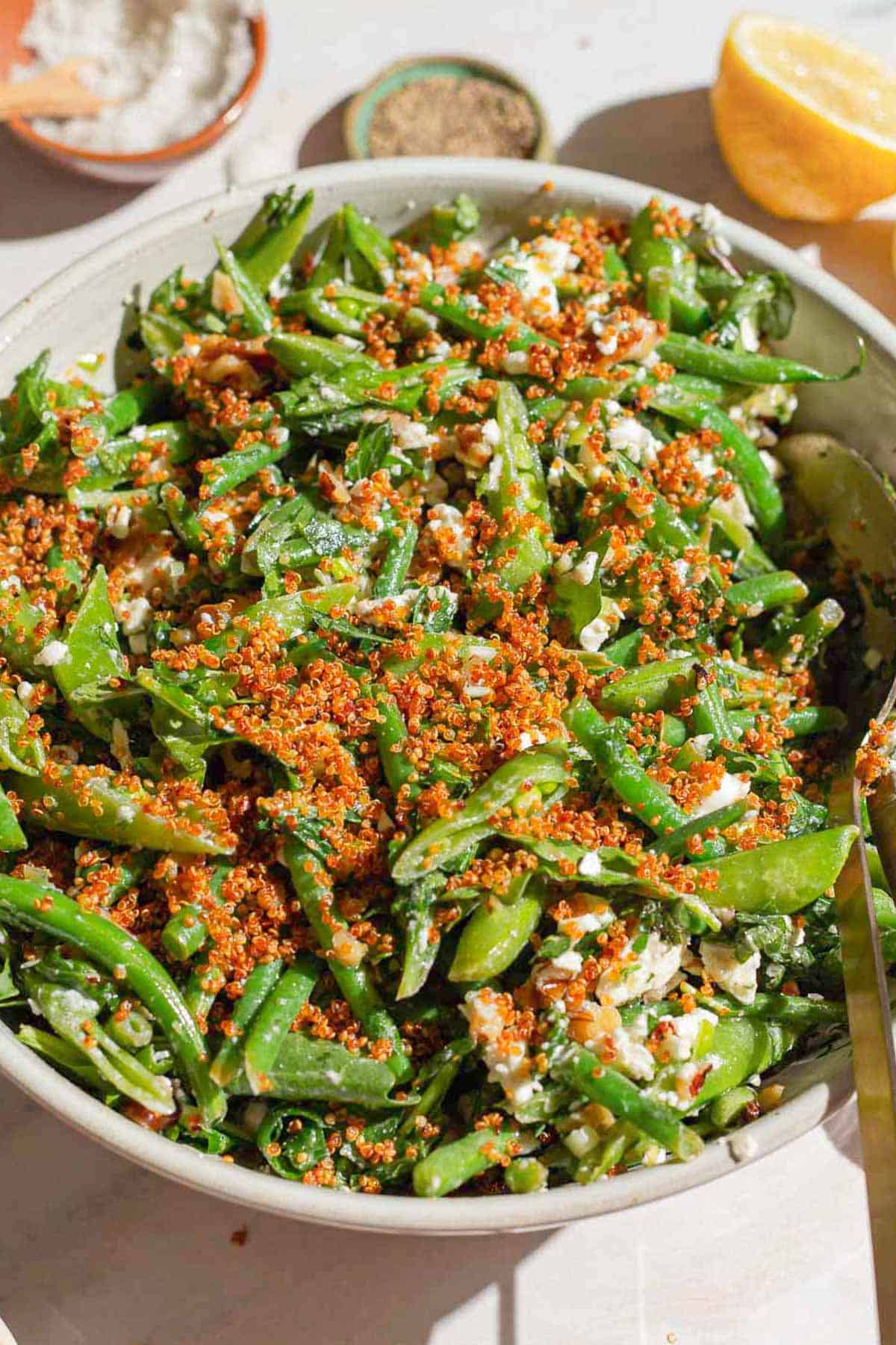 A close up of green bean and snap pea salad with crispy quinoa in a bowl with a spoon.