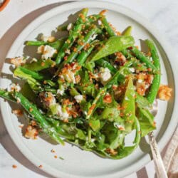 A close up of green bean and snap pea salad with crispy quinoa on a plate with a fork.