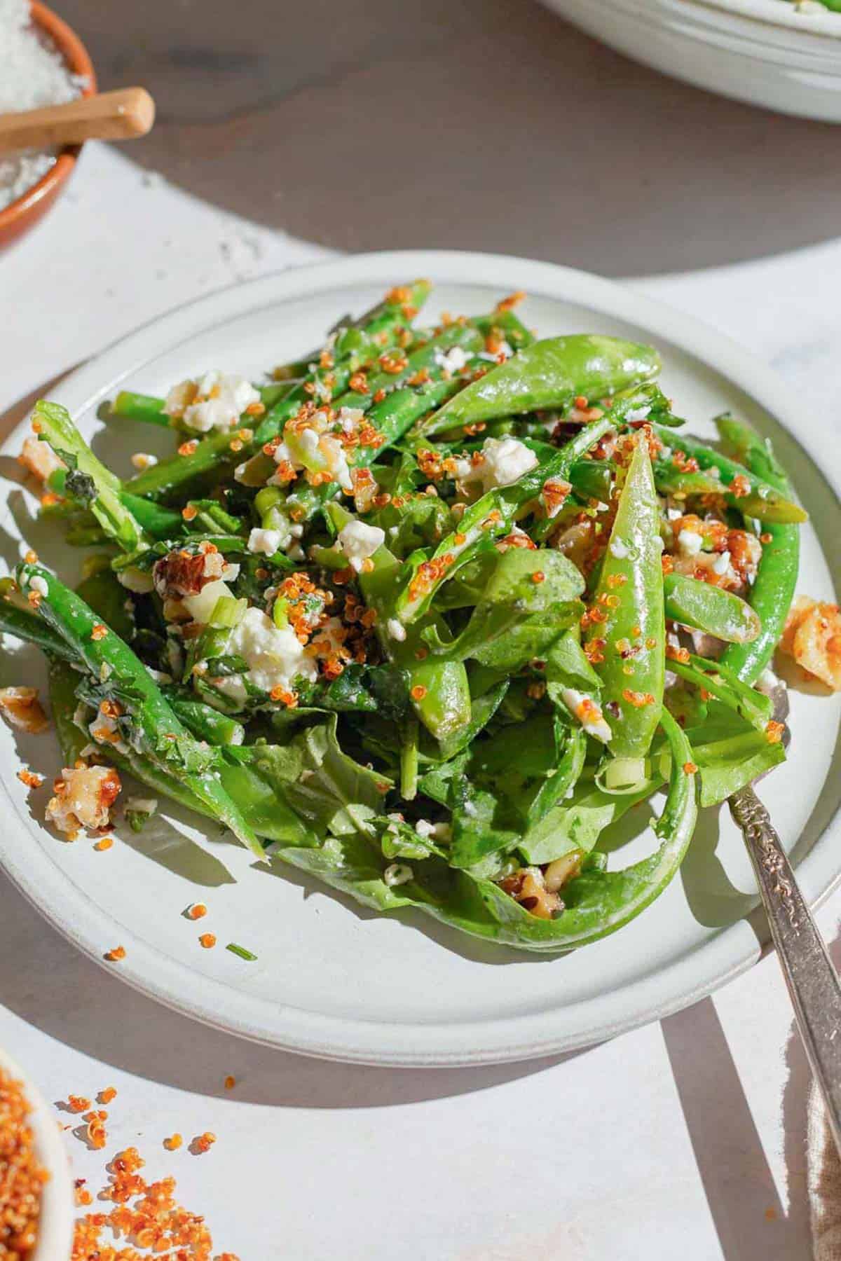 A close up of green bean and snap pea salad with crispy quinoa on a plate with a fork.