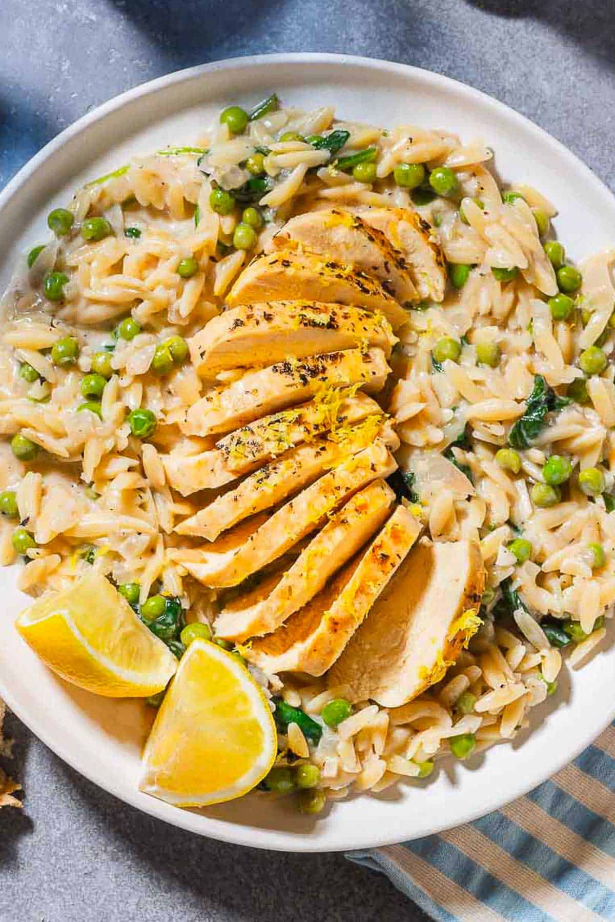 An overhead photo of a serving of lemon chicken orzo on a plate with lemon wedges.