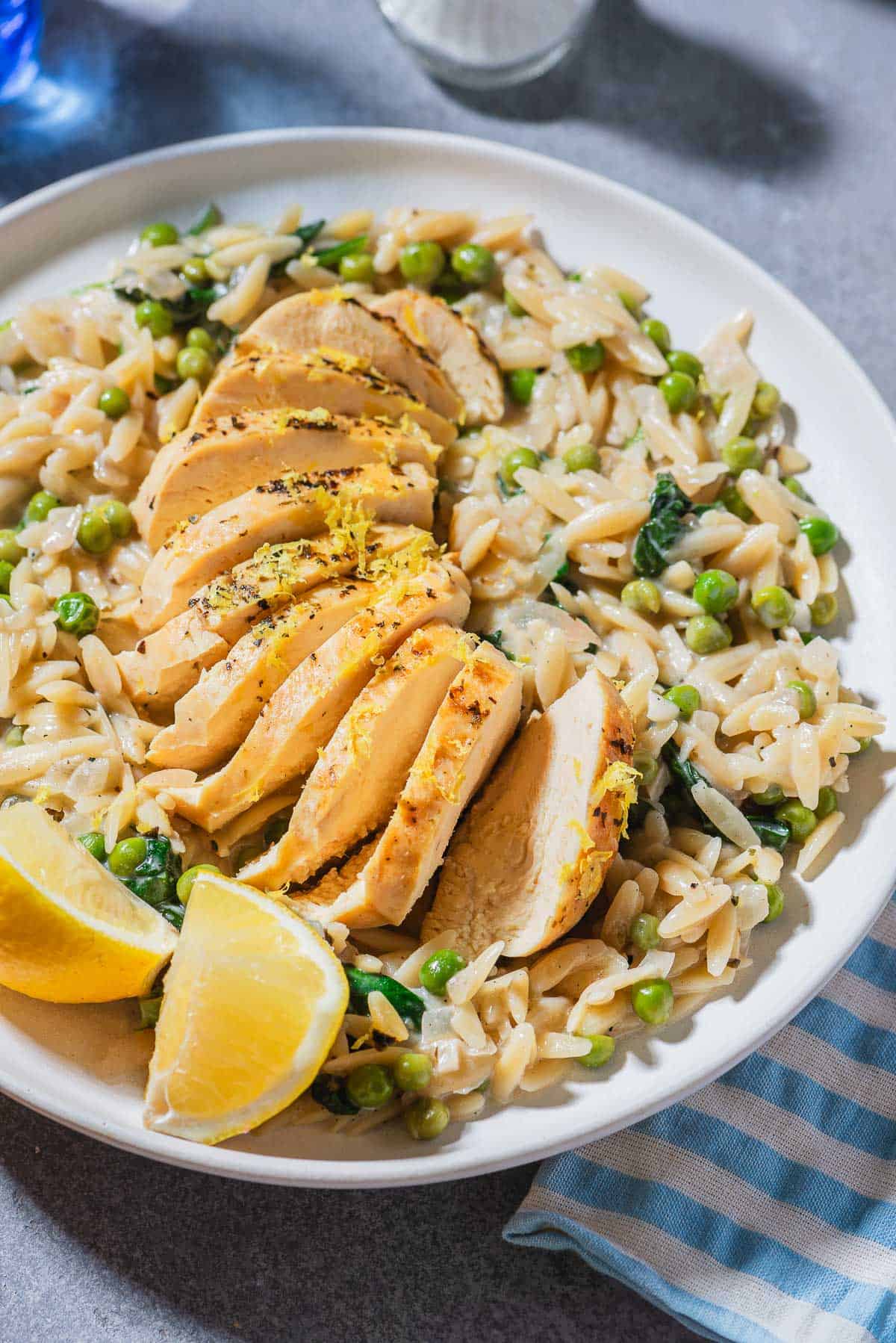 A close up of a serving of lemon chicken orzo on a plate with lemon wedges.