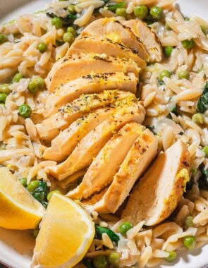 A close up of a serving of lemon chicken orzo on a plate with lemon wedges.