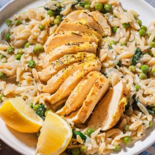 A close up of a serving of lemon chicken orzo on a plate with lemon wedges.