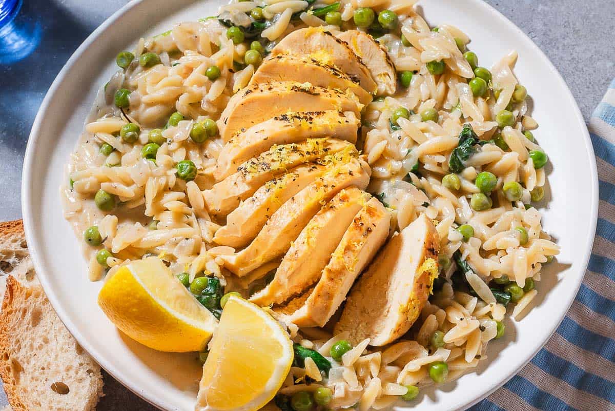 A close up of a serving of lemon chicken orzo on a plate with lemon wedges.