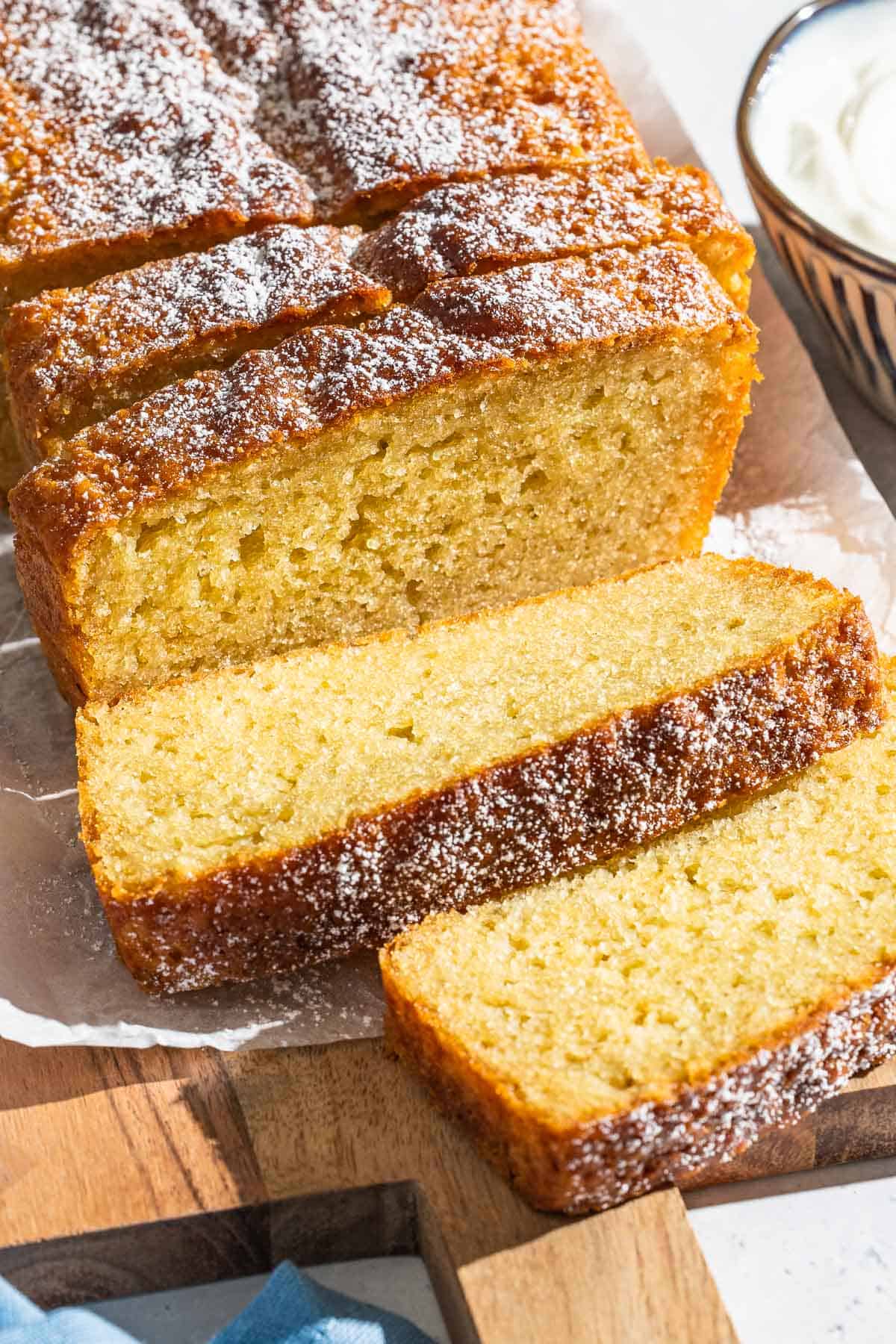 A close up of yogurt cake cut into slices on a parchment lined cutting board.