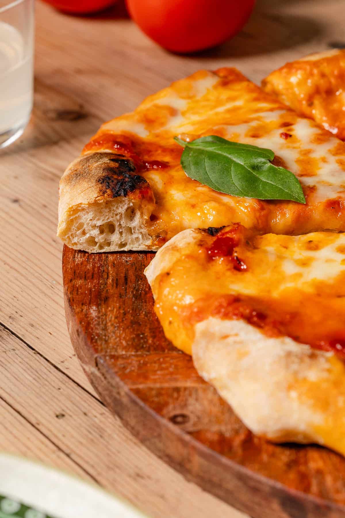 A close up photo of a sliced neapolitan pizza topped with basil leaves on a wooden platter.