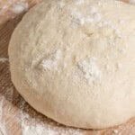 A close up of a ball of dough on a table dusted with flour.