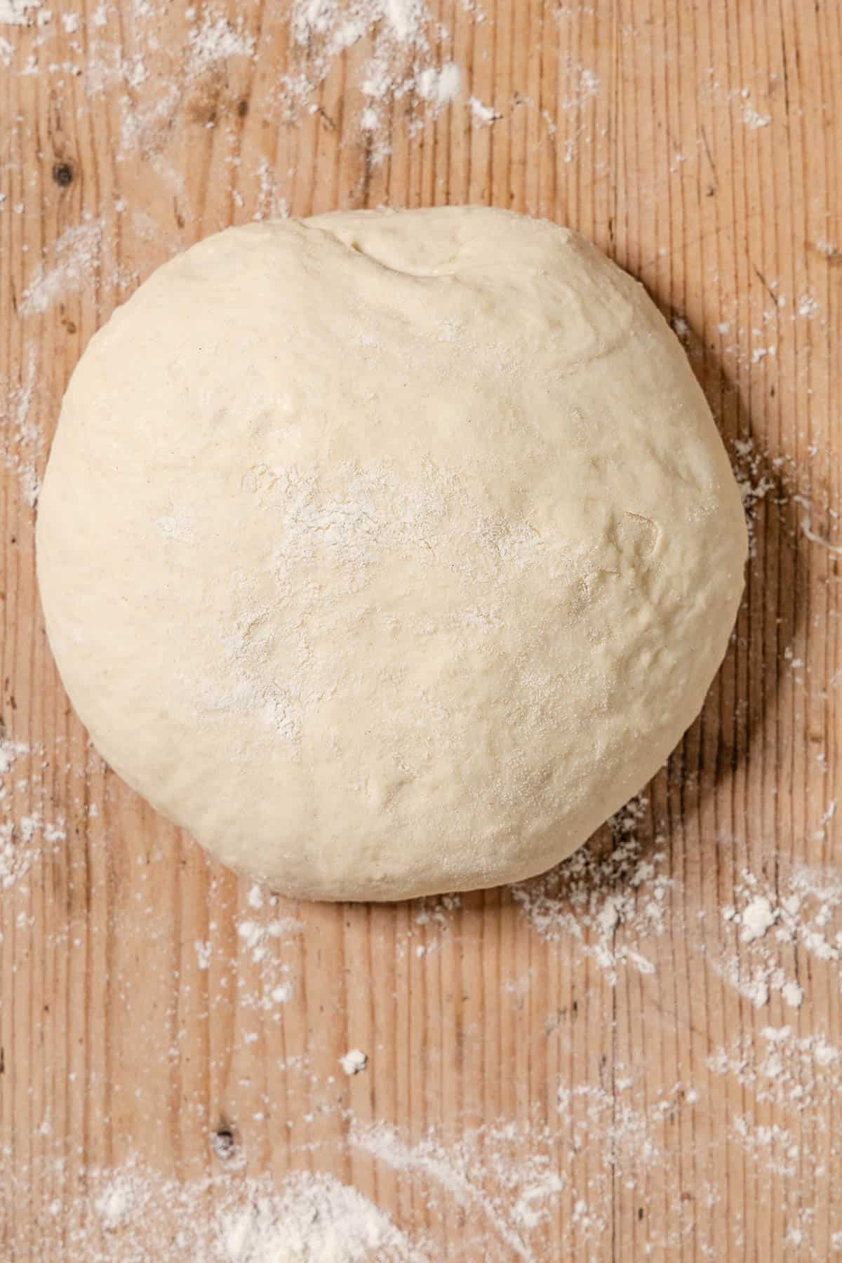 An overhead photo of a ball of dough on a table dusted with flour.