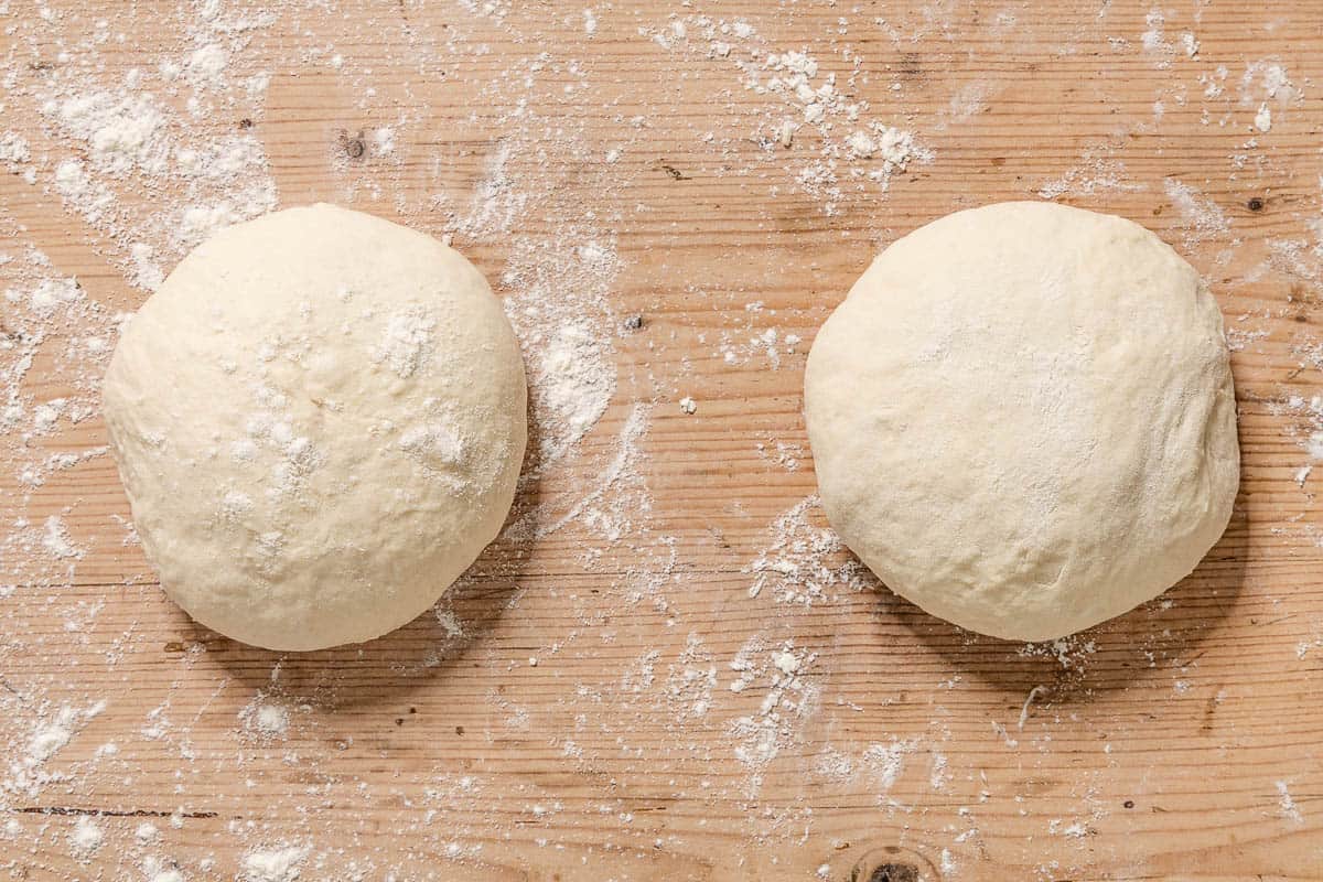 An overhead photo of two balls of dough on a table dusted with flour.