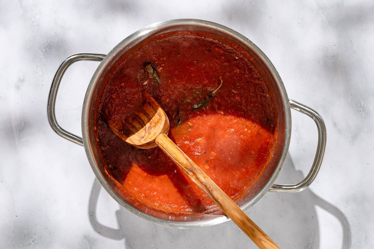 An overhead photo of the sauce for the tuna pizza simmering in a large pot with a wooden spoon.