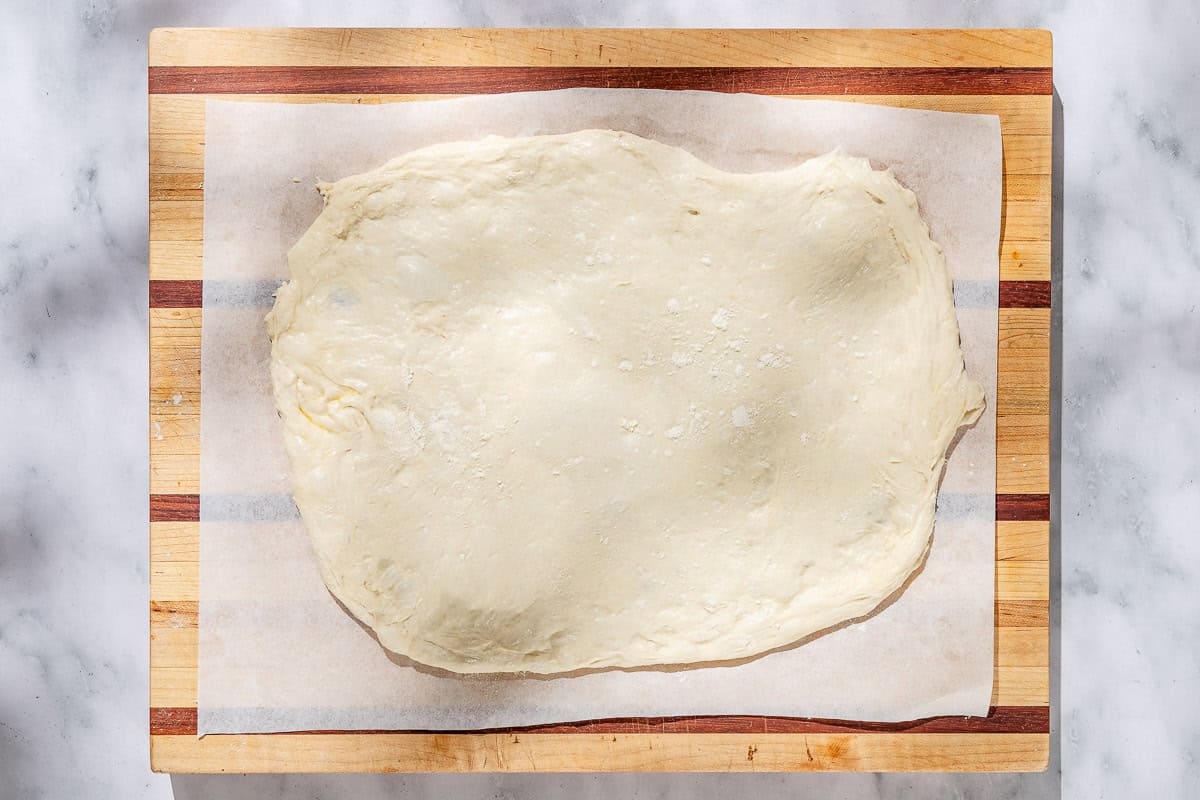 Neapolitan-style pizza dough spread rolled into an oval shape on a parchment lined cutting board.