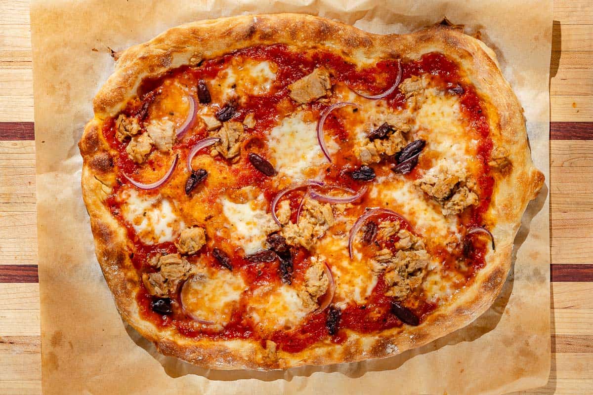 An overhead photo of tuna pizza on a piece of parchment paper on a wooden cutting board.