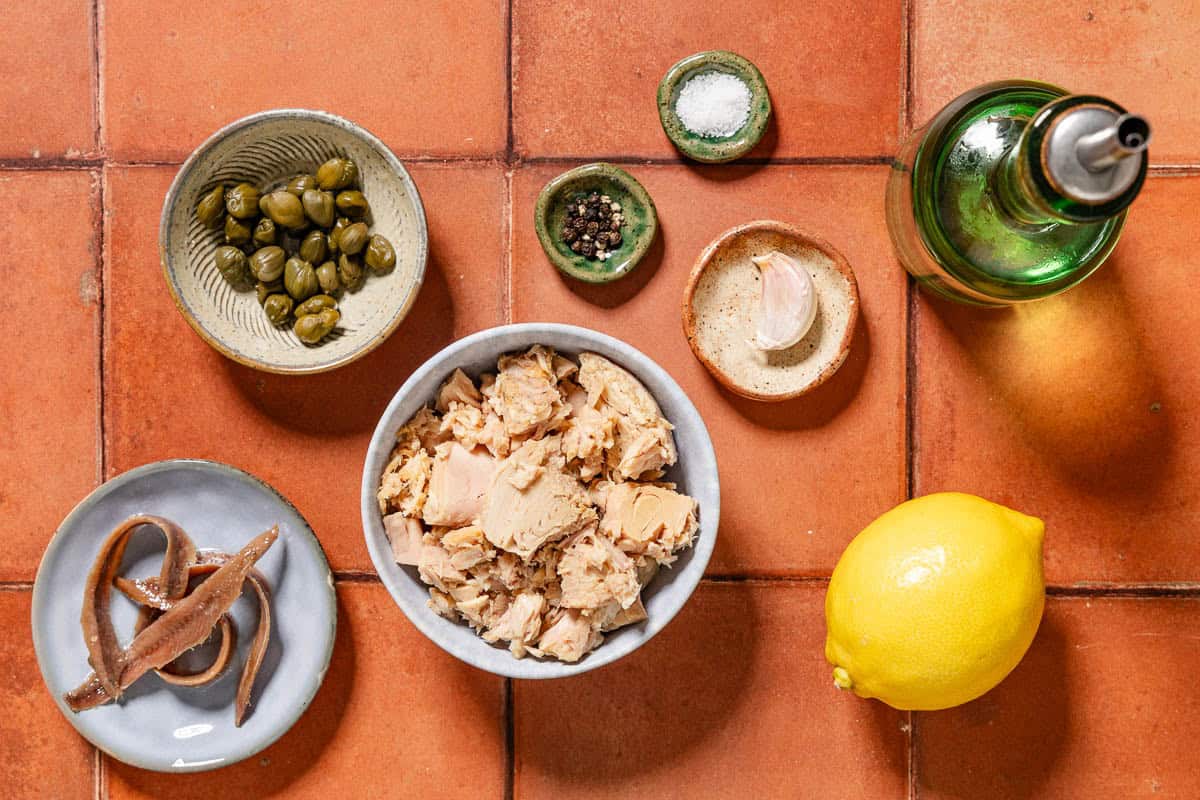 Ingredients for tonnato sauce including tuna, anchovies, capers, garlic, lemon, olive oil, salt and black pepper.