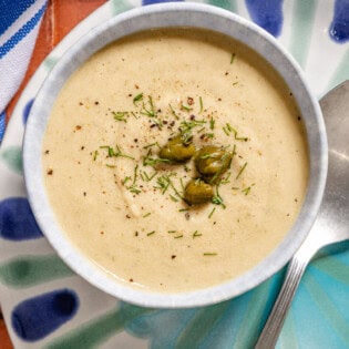 An overhead photo of a bowl of tonnato sauce topped with dill and capers on a plate with a spoon.