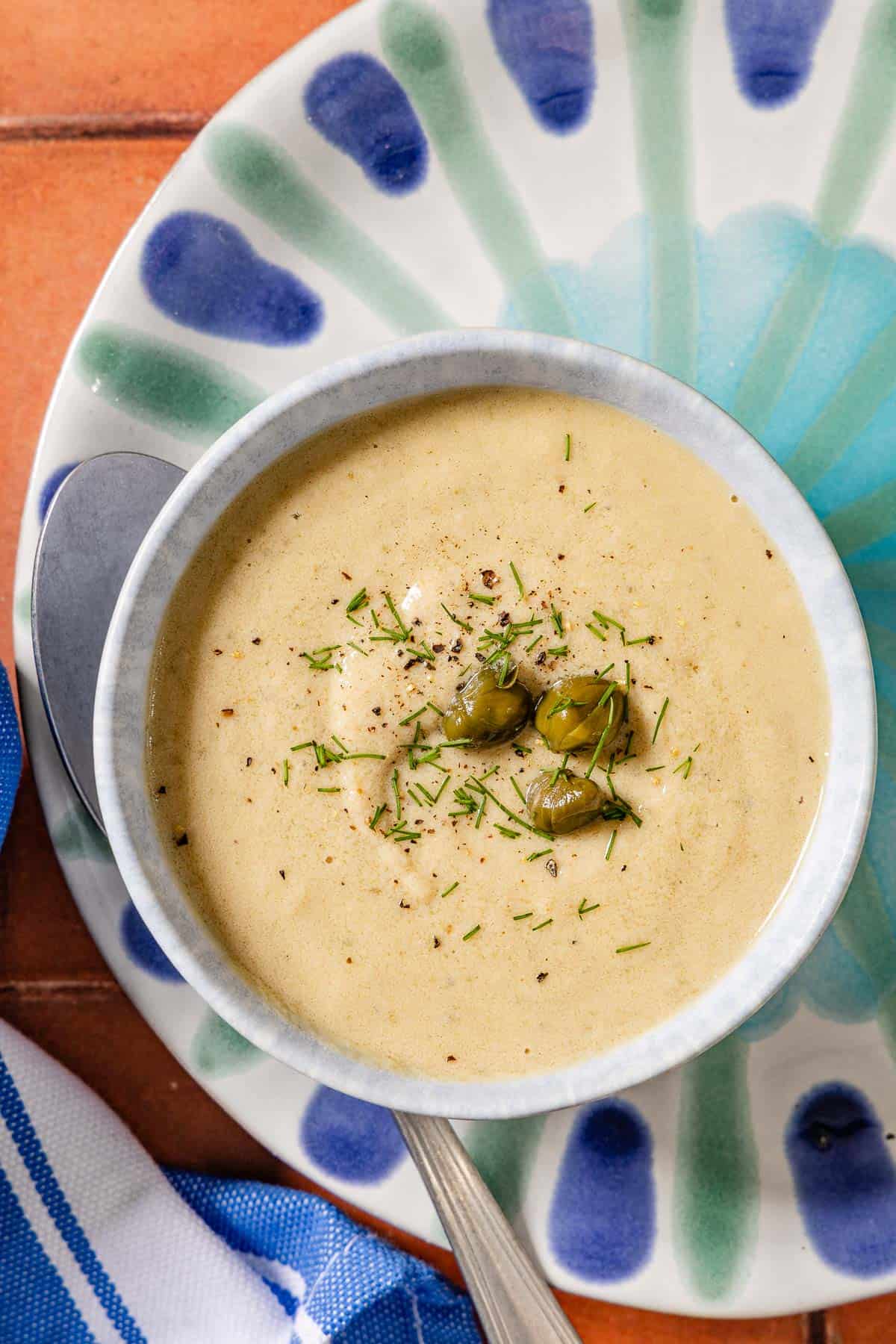 An overhead photo of a bowl of tonnato sauce topped with dill and capers on a plate with a spoon.