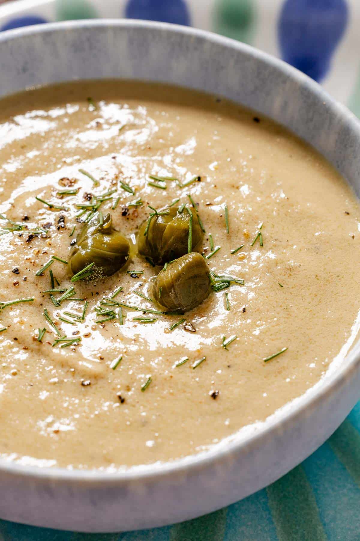 A close up of a bowl of tonnato sauce topped with dill and capers.