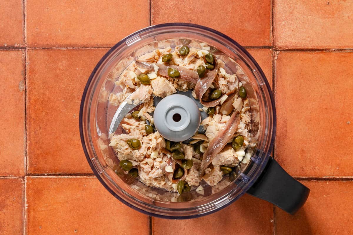 The ingredients for tonnato sauce in the bowl of a food processor fitted with a blade just before being mixed together.