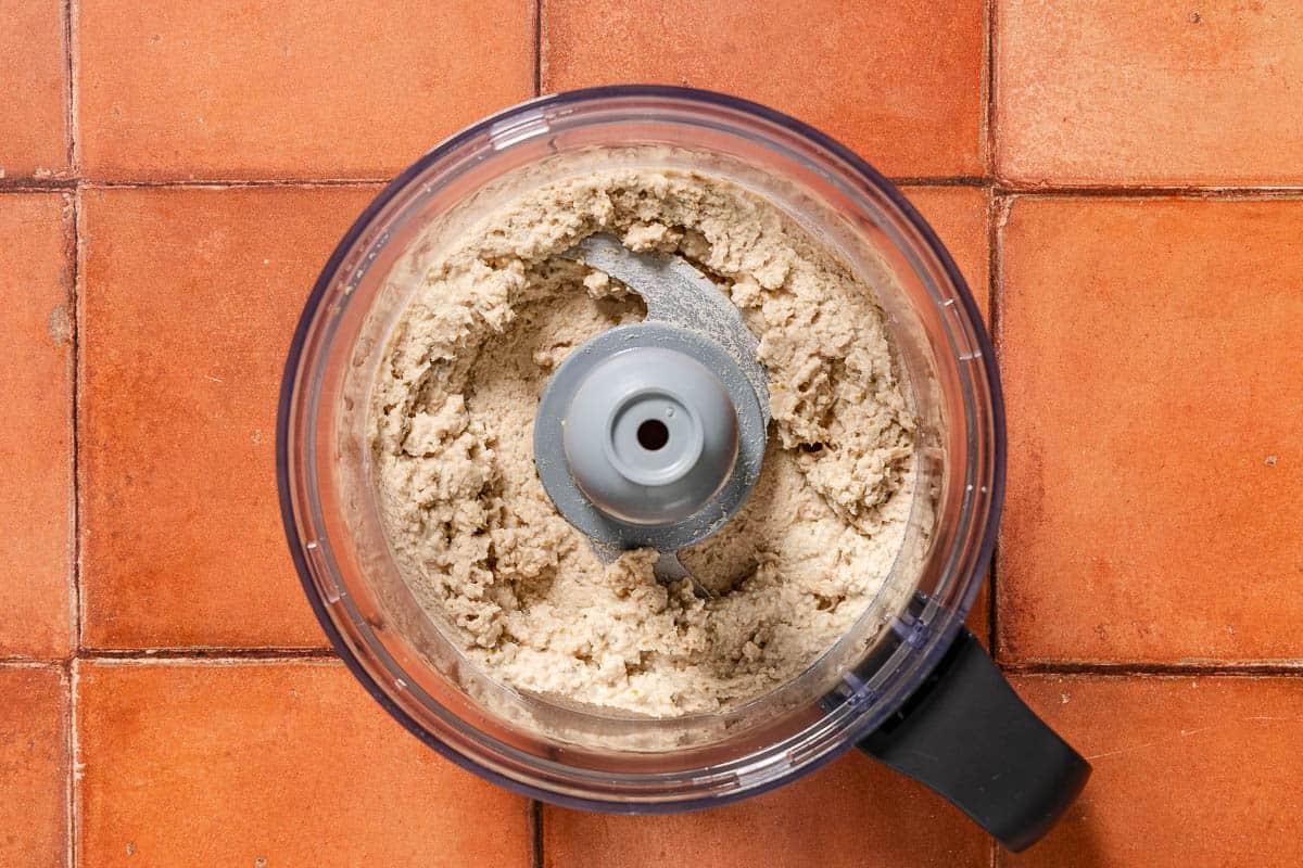 The tonnato sauce in the bowl of a food processor fitted with a blade.