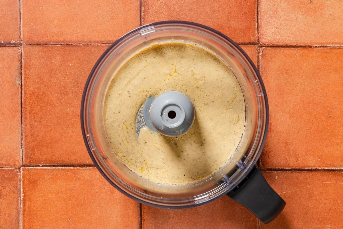 The tonnato sauce in the bowl of a food processor fitted with a blade.