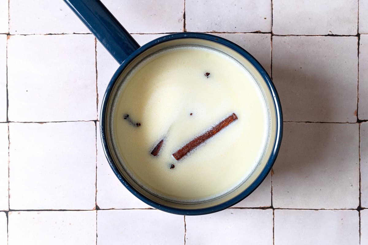 Milk and half and half being flavored with vanilla extract , cinnamon sticks and cloves in a saucepan.