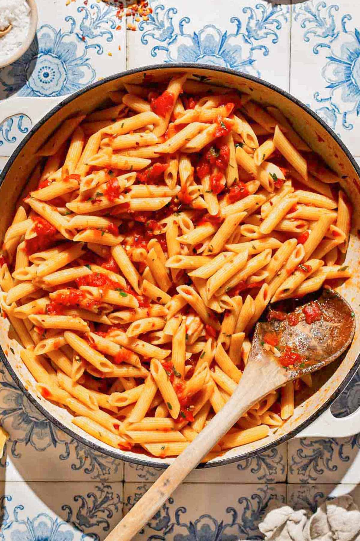 An overhead photo of arrabbiata sauce pasta in a skillet with a wooden spoon.