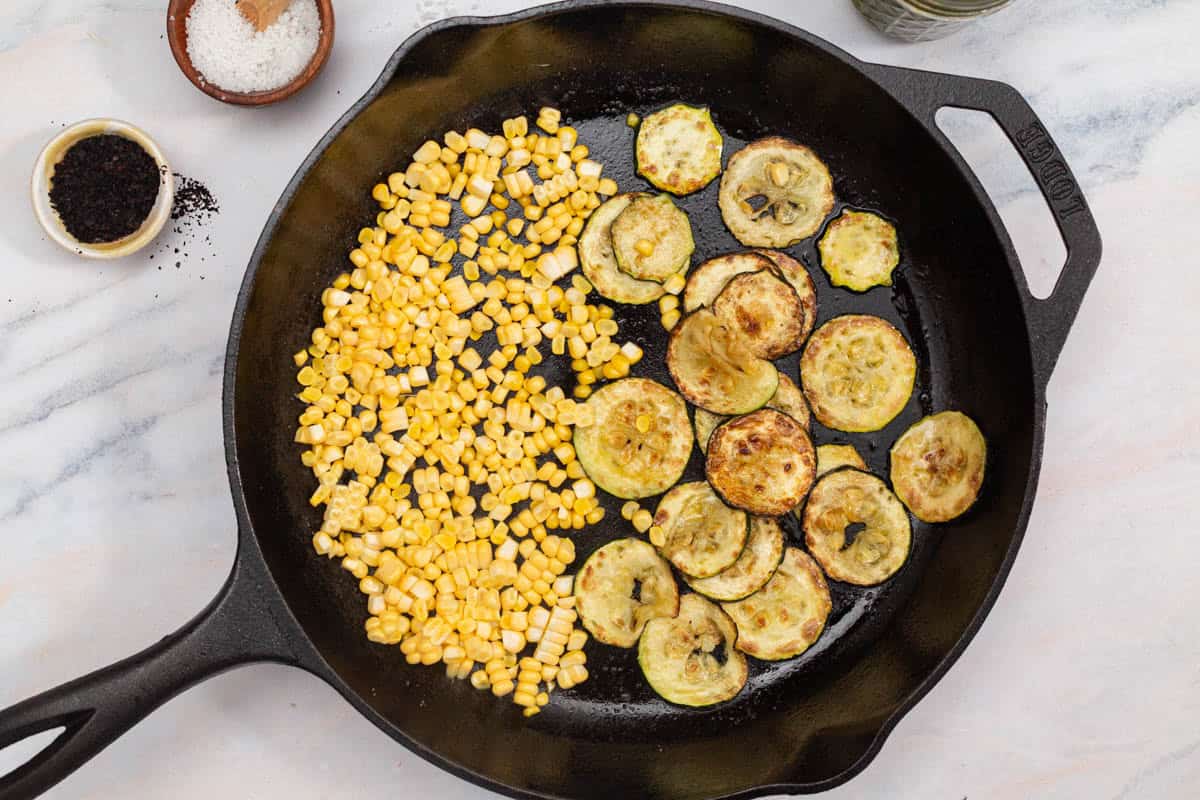 An overhead photo of slices of zucchini and corn kernels being sauteed in a cast iron skillet. Next to this are bowls of salt and urfa biber.