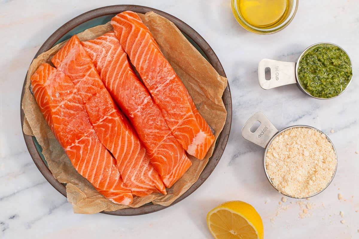 Ingredients for pesto salmon including 4 salmon fillets, panko breadcrumbs, olive oil, basil pesto, and lemon.