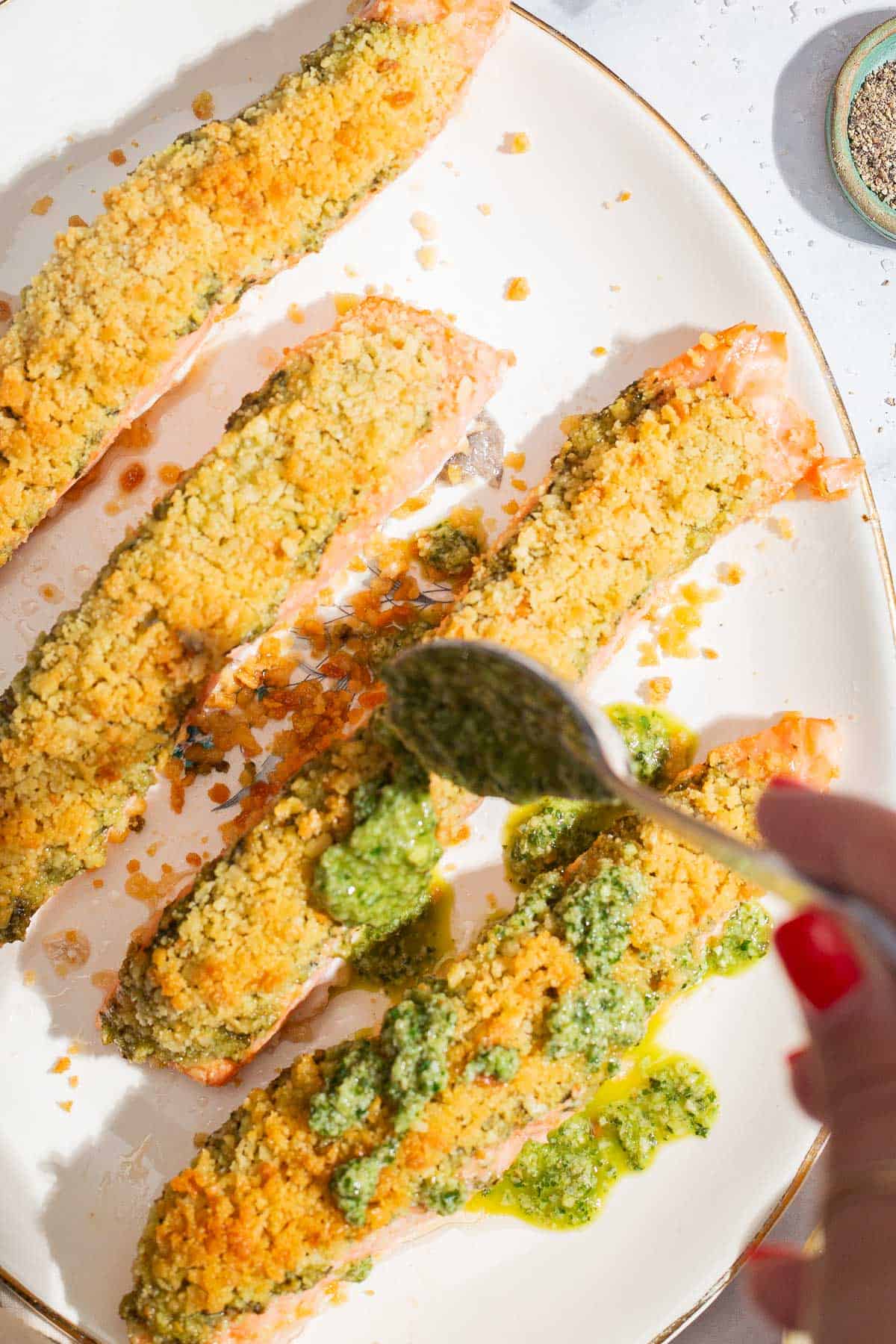 An overhead photo of pesto being drizzled on to the 4 salmon fillets on a platter.