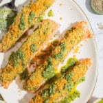 An overhead photo of 4 pesto salmon fillets on a platter with a spoon. Next to this are bowls of salt, pepper and pesto.