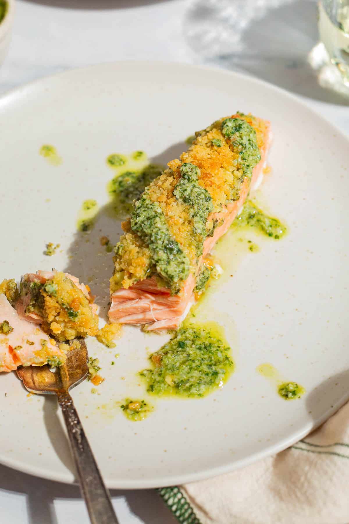 A close up of a pesto salmon fillet on a plate with a fork.