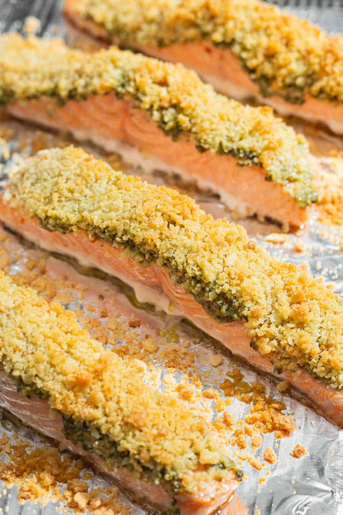 4 pesto salmon fillets on a baking sheet lined with aluminum foil.