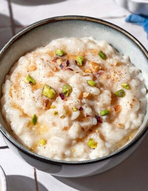 A close up of easy rice pudding garnished with pistachios, walnuts, cinnamon and a drizzle of honey.