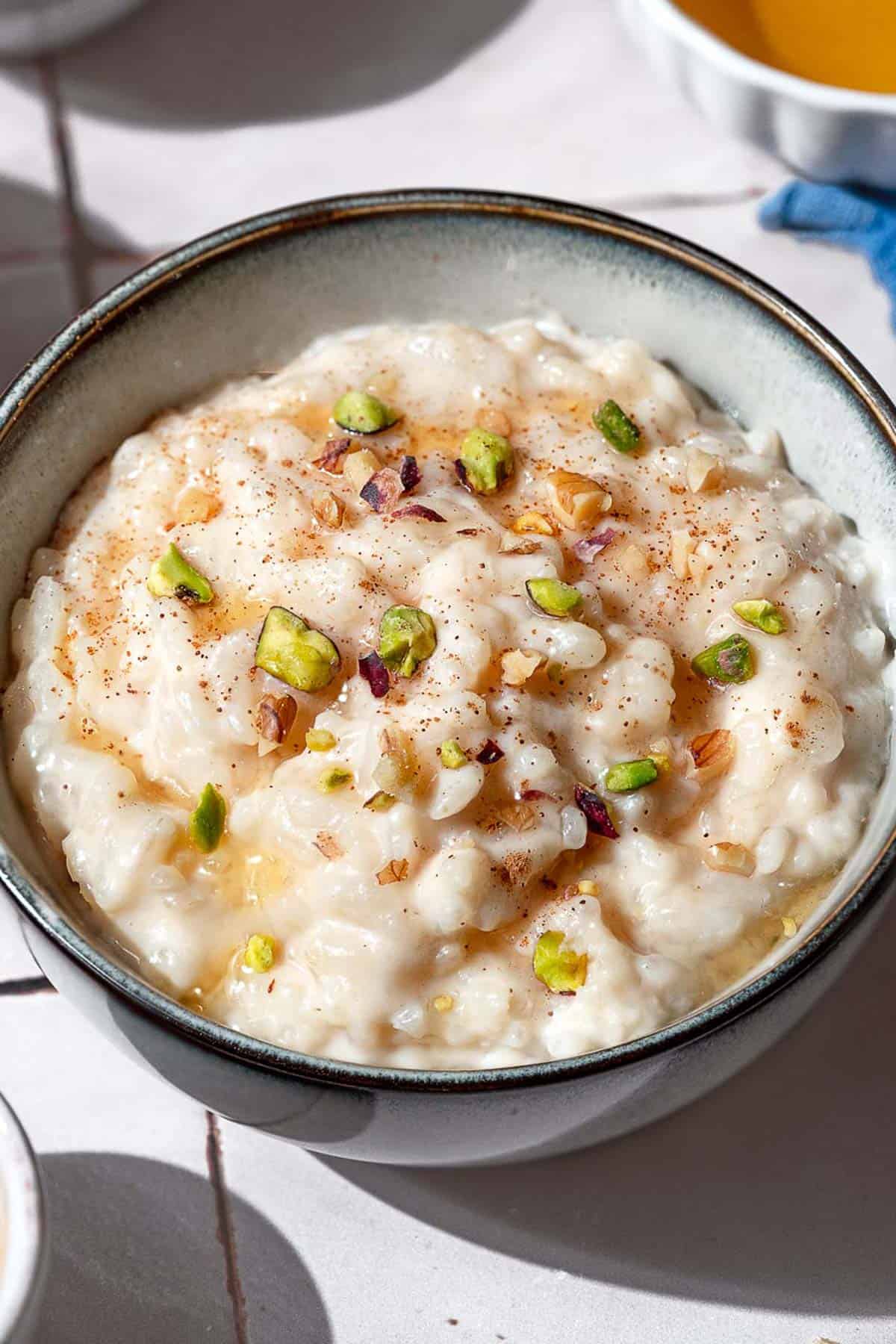 A close up of easy rice pudding garnished with pistachios, walnuts, cinnamon and a drizzle of honey.