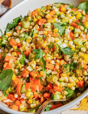 A close up of grilled corn salad in a serving bowl with a spoon. Next to this is a cloth napkin and small bowls of salt and cumin.