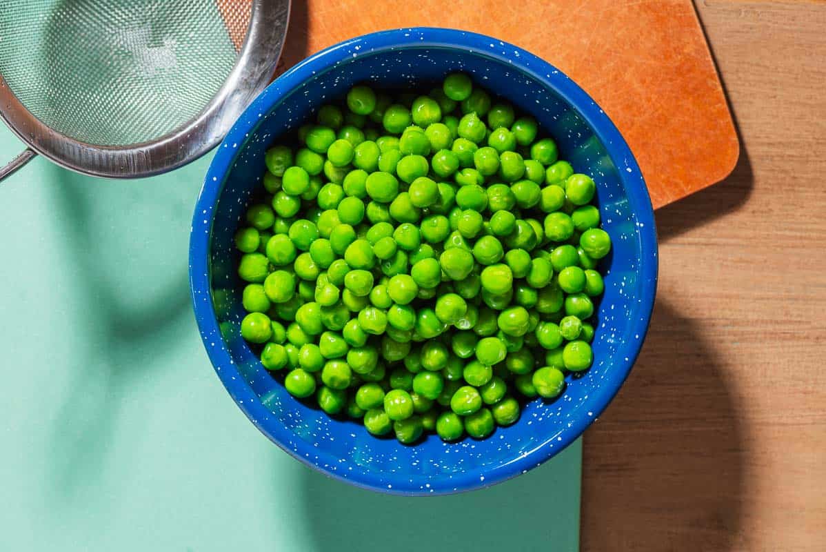 A close up of a bowl of peas next to a strainer.