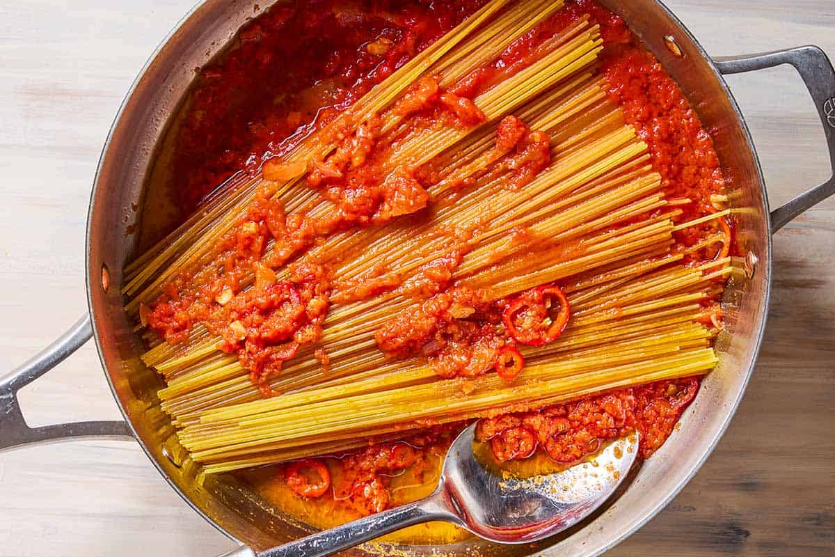 An overhead photo of the spaghetti being coated in the tomato sauce in a skillet with a spoon.