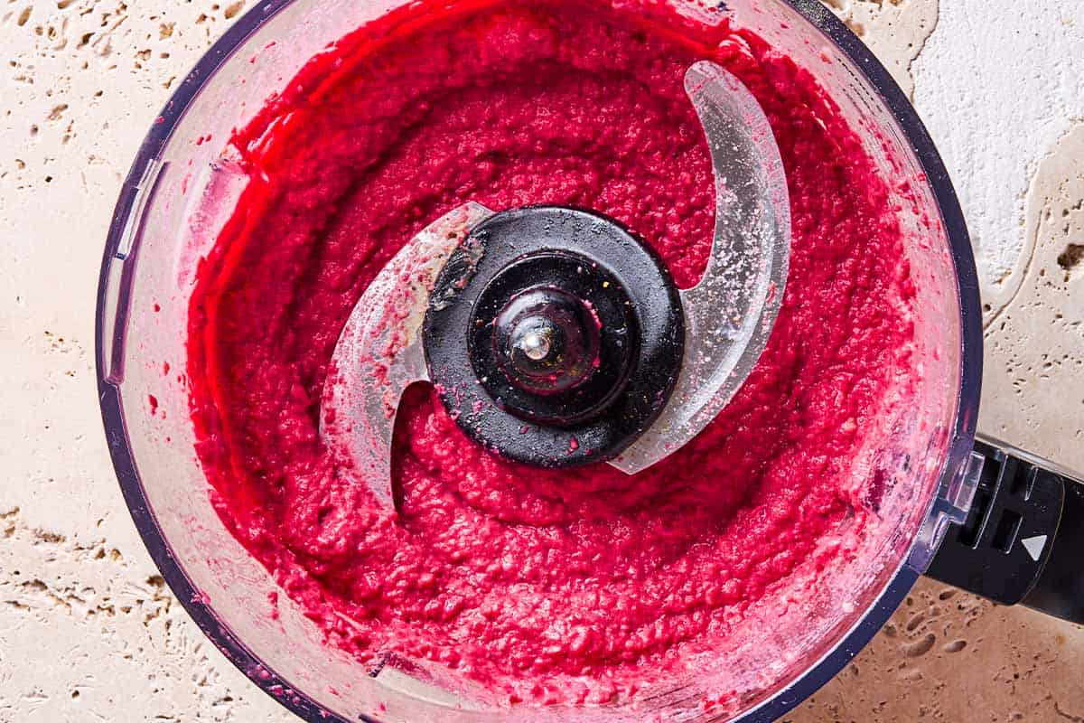 beet hummus in the bowl of a food processor fitted with a blade.