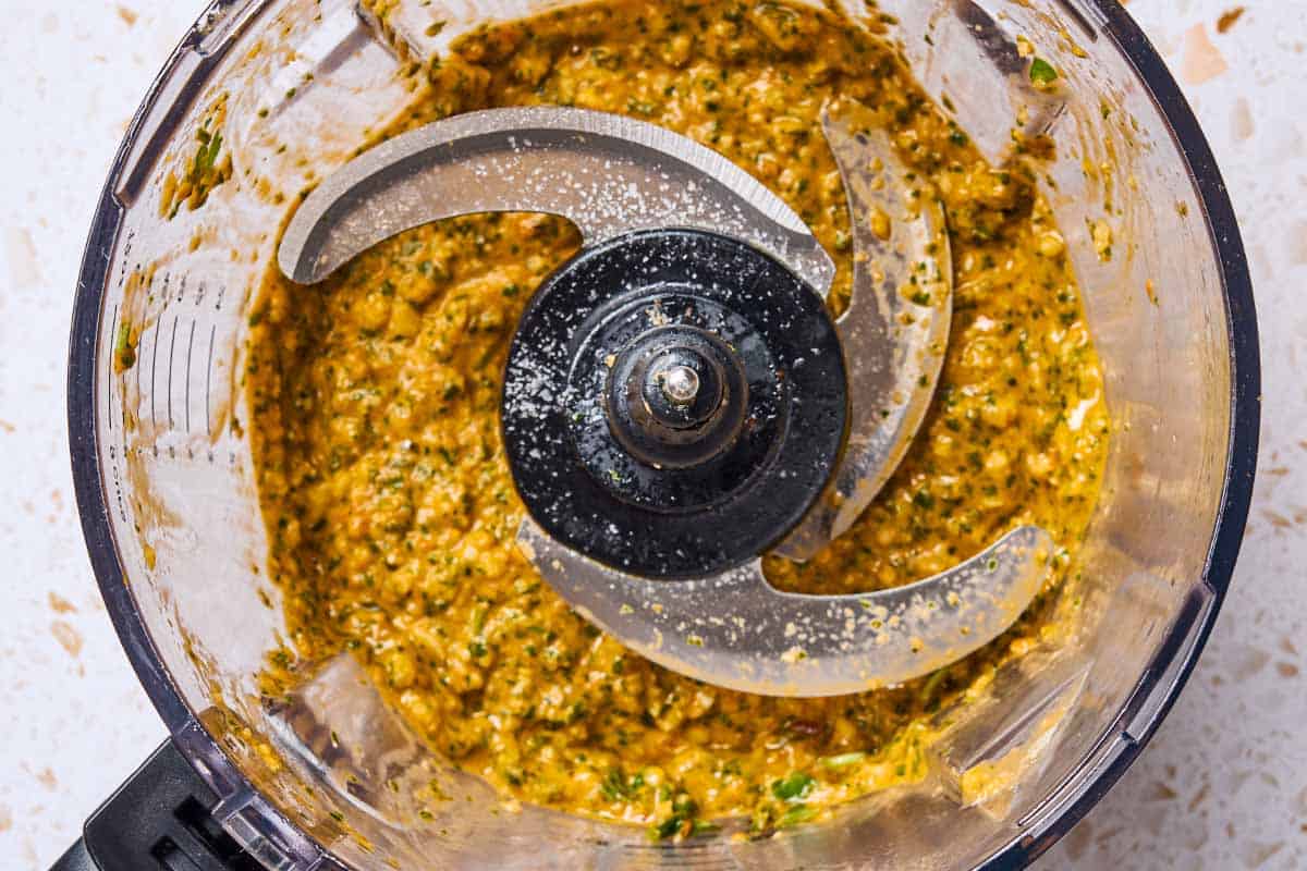 An overhead photo of An overhead photo of pesto alla trapanese in the bowl of a food processor fitted with a blade.