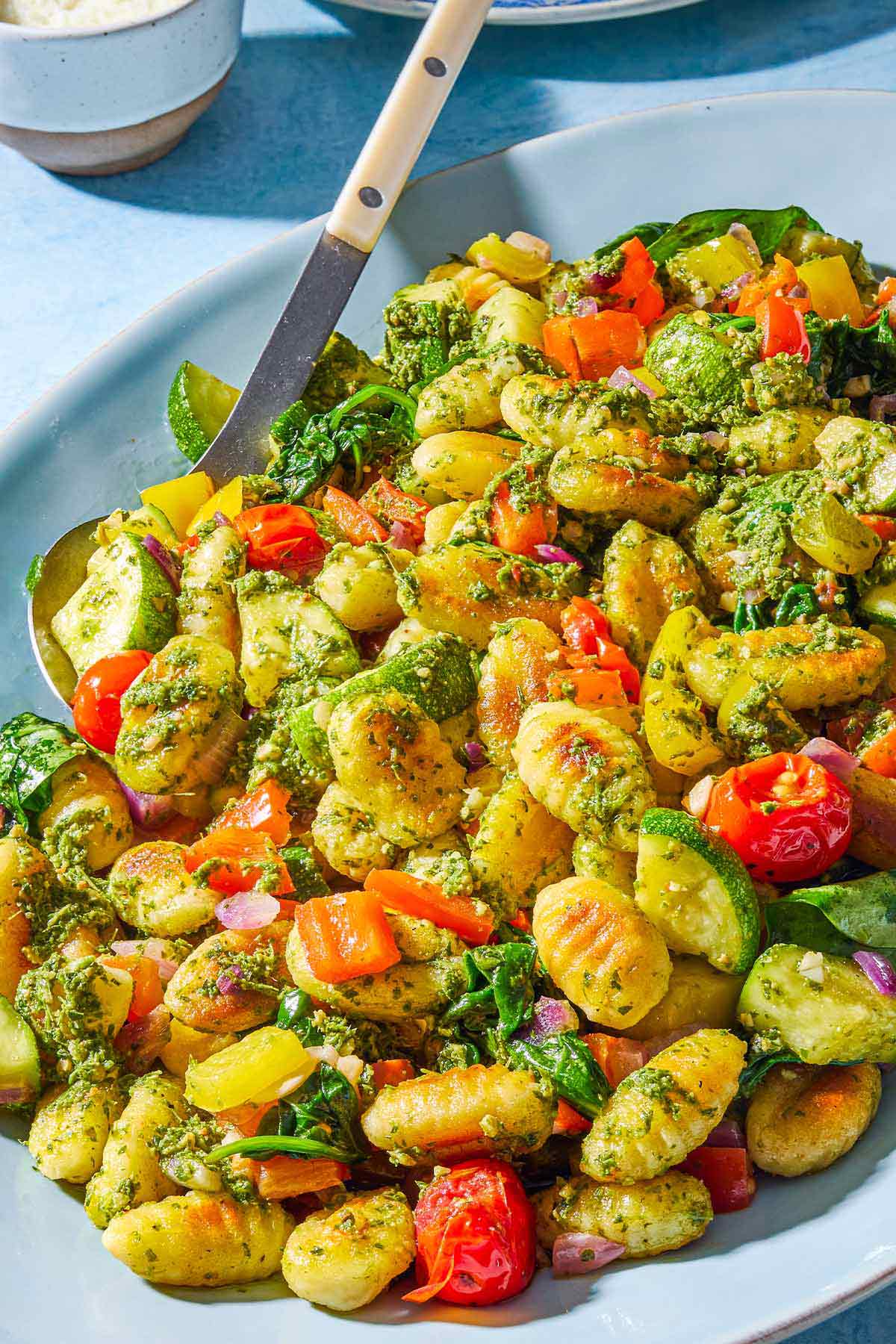 A close up of crispy gnocchi with pesto on a serving platter with a spoon.