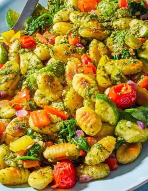 A close up photo of crispy gnocchi with pesto on a serving platter with a spoon.